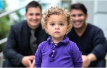 Curly-haired boy standing in front of his adoptive fathers